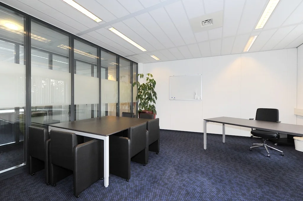 Moderne kantoorruimte aan de Laan van S-Gravenmade met vergadertafel, bureau en glazen scheidingswand.